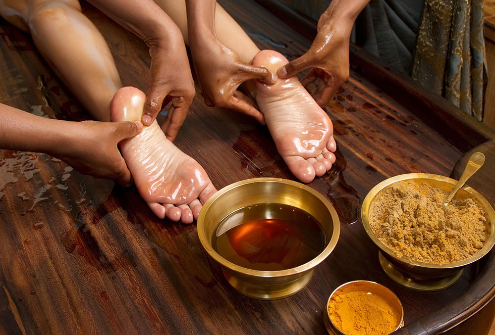 Ayurvedic therapist performing Padabhyanga foot massage with warm herbal oils